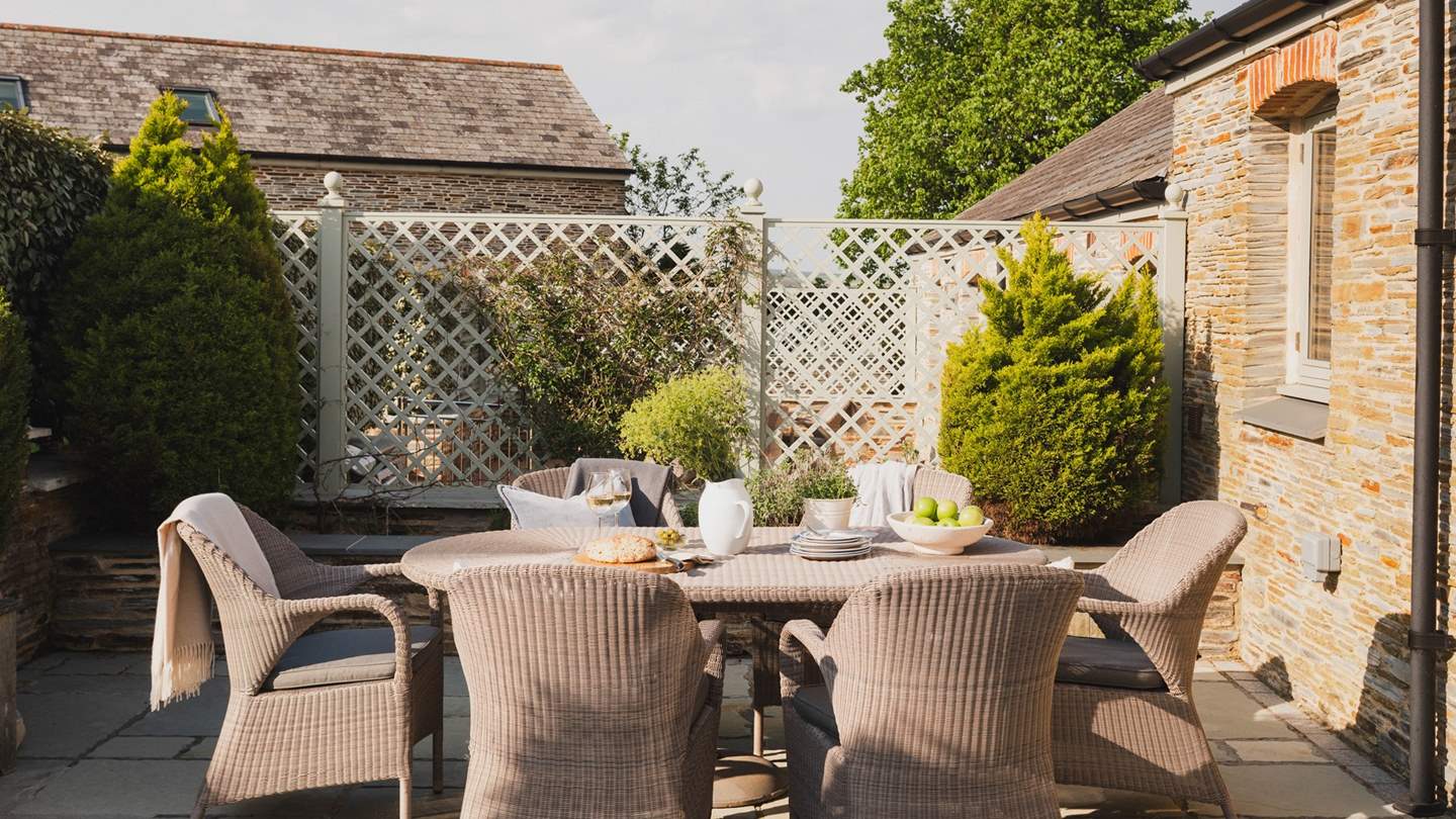 Steps lead down to a large front patio with outdoor dining furniture and gas barbecue