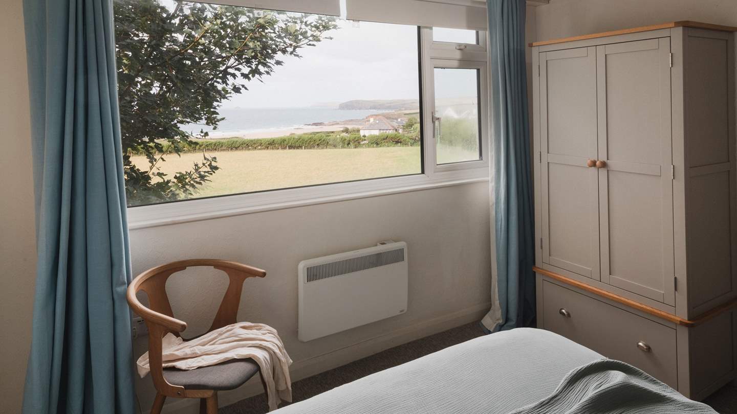 Benefitting from lots of natural light, this peaceful bedroom enjoys generous windows framing fields that meet with grass-tufted dunes 