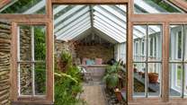 More relaxing space is found in the beautiful old greenhouse, where a table and chairs and a padded bench seat make the perfect place for morning coffee on breezier days.