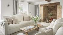 The exquisite sitting room is resplendent in pale, calming shades with original beams and the large inglenook fireplace