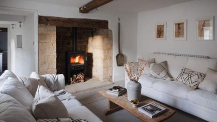The beautiful sitting room is resplendent in pale, calming shades with original beams and the large inglenook fireplace complete with a cosy wood burner