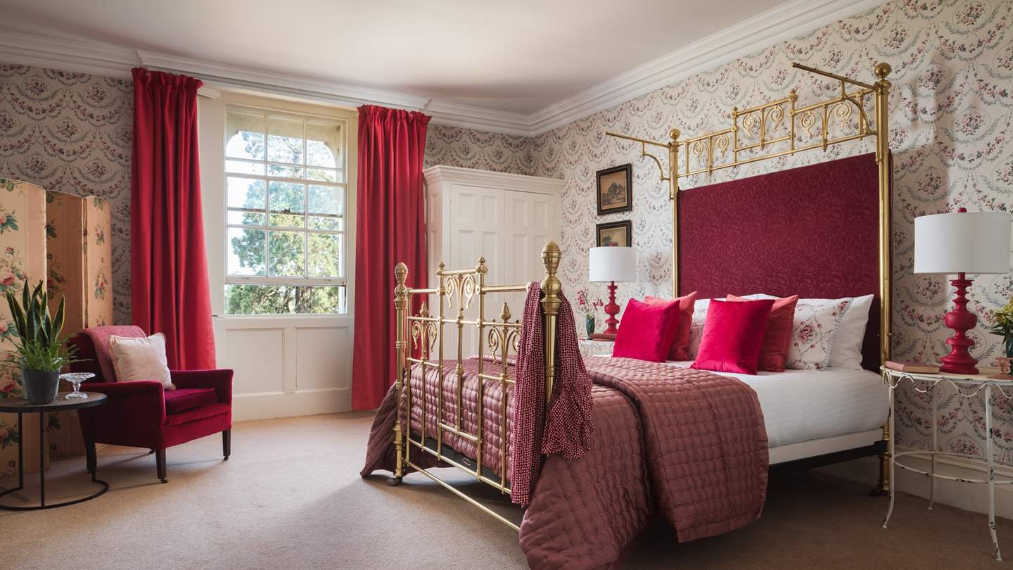The red bedroom boasts a king-sized brass bed with built in wardrobe, original feature fireplace and antique artwork