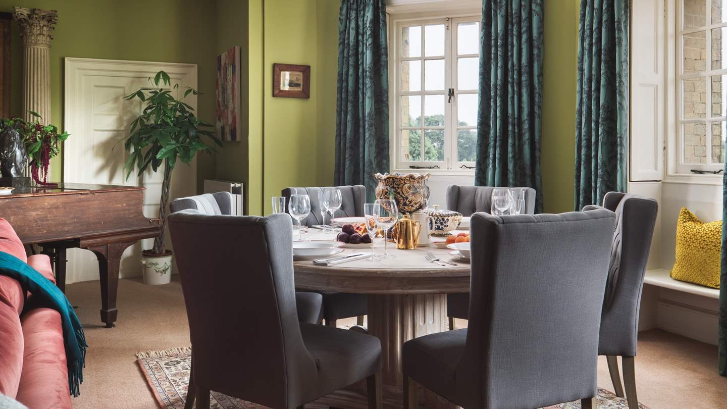 To the back of the room, close to the window, is the large circular dining table seating six