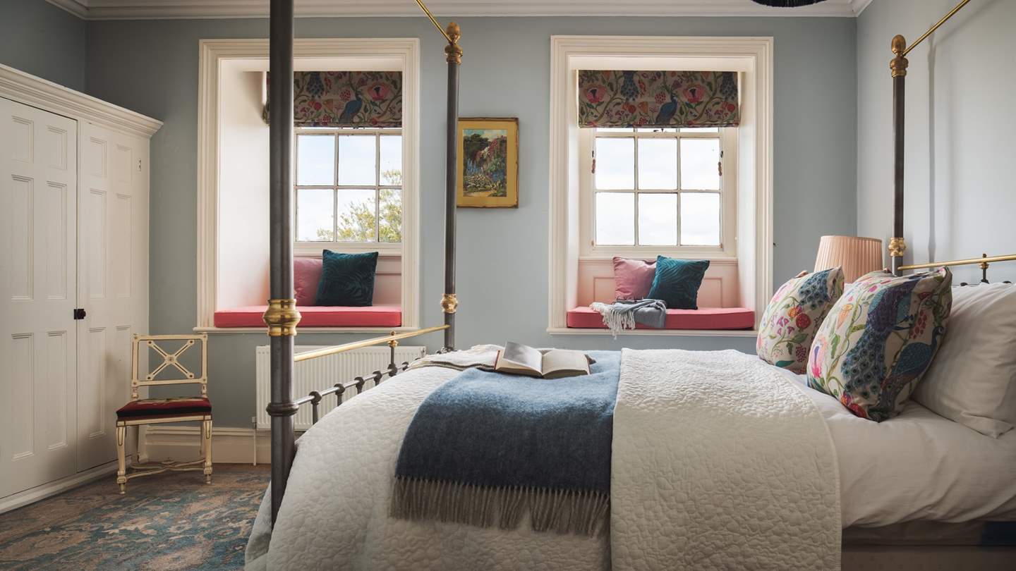 The cosy blue bedroom has a king-sized four poster bed, two window seats with garden views and a built-in wardrobe