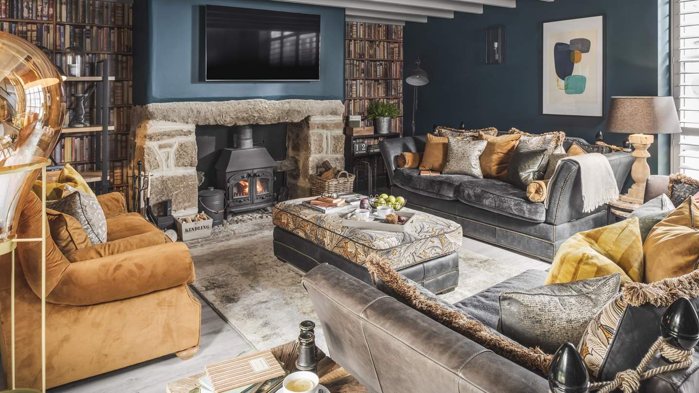 The elegant sitting room in shades of teal, grey and gold is home to sumptuous sofas nestling around the flickering wood burner