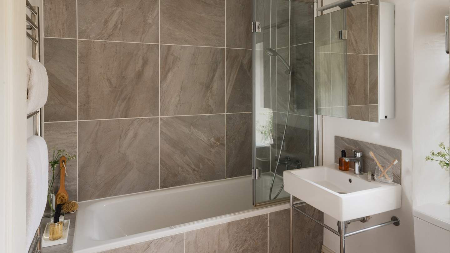 The family bathroom in shades of grey and white has a gorgeously deep bath for long soaks with a shower overhead