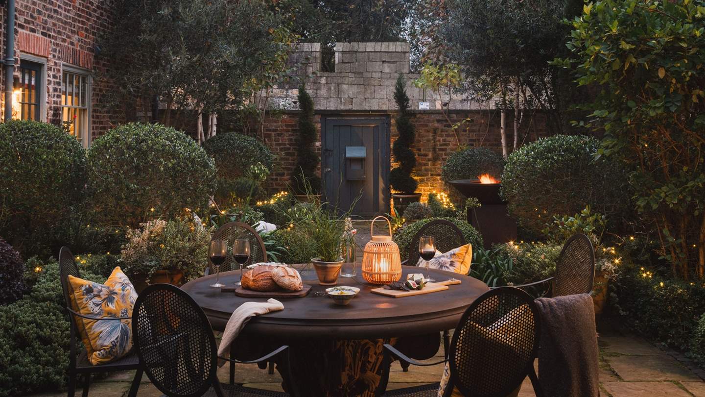 The outdoor table for four is beautifully bordered by manicured hedges - a divine setting after dusk