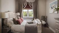 The master bedroom holds a lavish king size bed adorned in gorgeous linens, throws and cushions