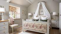 The second bedroom is light and bright, with a sumptuous king-sized bed with drapes 