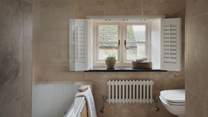 The lovely family bathroom with marbled tiling and elegant French shutter windows can be found upstairs, complete with a bathtub and an overhead shower