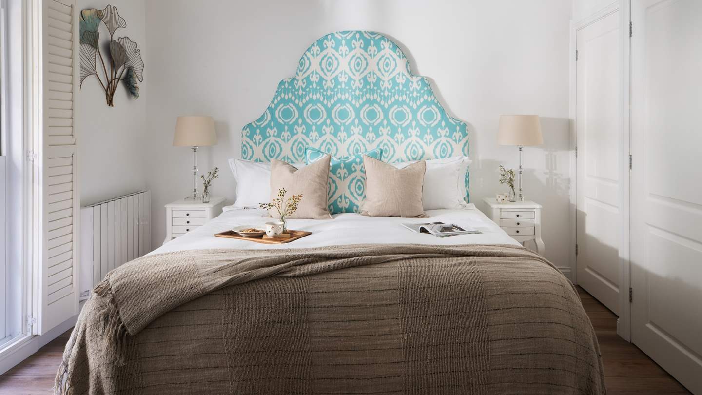 The master bedroom features a striking teal patterned headboard, adding a touch of colour to this neutral, calming space 