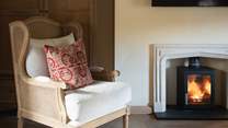 A charming occasional chair rests beside the wood burning stove, providing a lovely spot for moments of serene quietude...