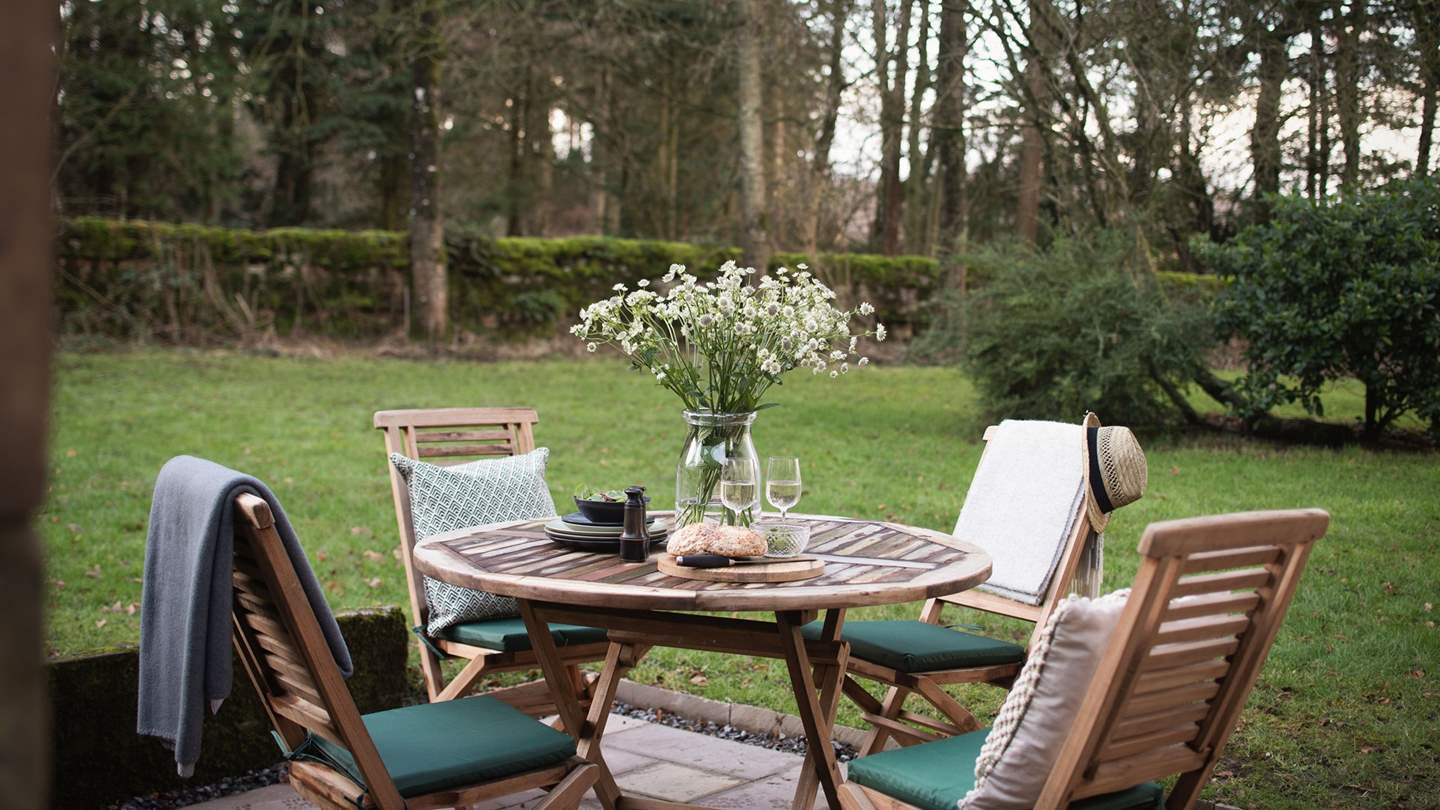 A teak garden table and chairs provide an enchanting setting for alfresco evening dining