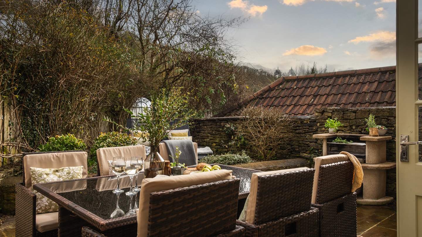 Ready for alfresco meals, a large, glass-topped table for six rests on the patio, surrounded by comfy wicker chairs and an outdoor BBQ