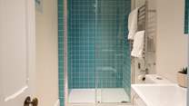 The second bedroom also has an ensuite shower room with teal blue tiles and a large rainfall shower