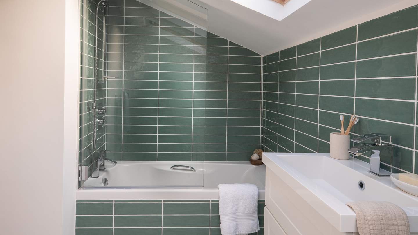 The top floor family bathroom has fetching green tiles and a bath with an overhead shower