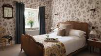 On the walls is Sicilia Wallpaper by Lewis & Wood, while draped across the bed are homely pillows and throws for extra hygge