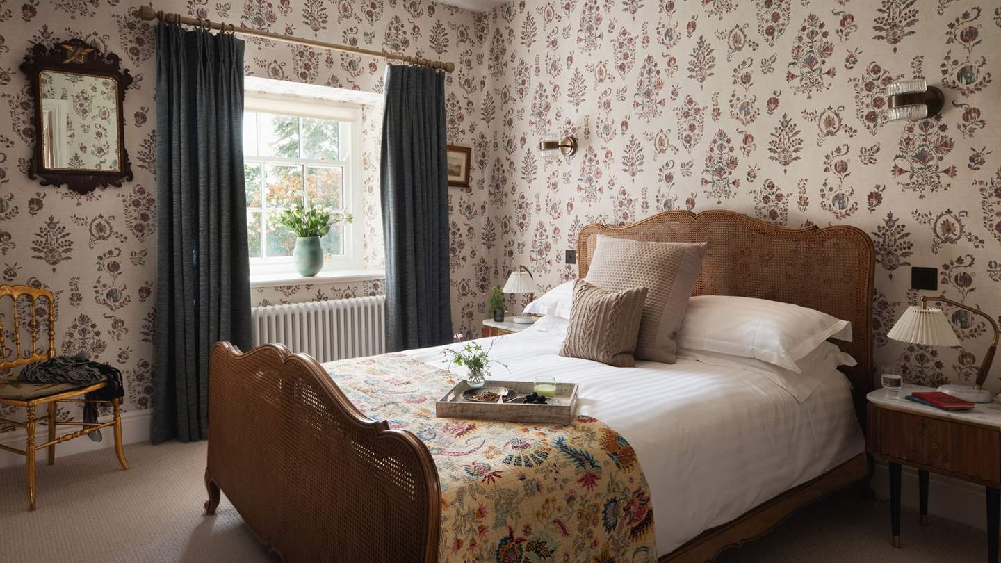 On the walls is Sicilia Wallpaper by Lewis & Wood, while draped across the bed are homely pillows and throws for extra hygge