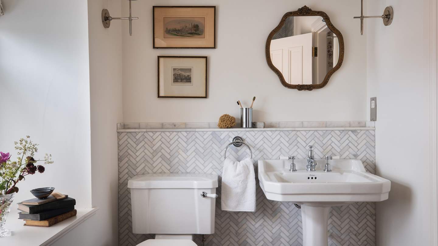 This bathroom is dressed in herringbone marble tiles and white walls and has its own walk-in shower