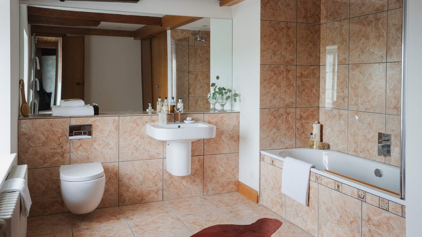 This bedroom is complemented by a spacious ensuite bathroom with terracotta-hued marbled tiles and a bath with a shower overhead