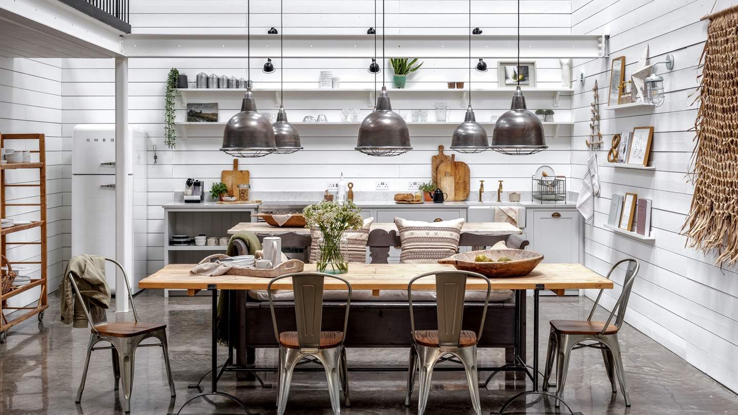 For dining in comfort and style, an oversized table with a vintage two-seater bench and four chairs reside under industrial pendant lights, ready for feasting together