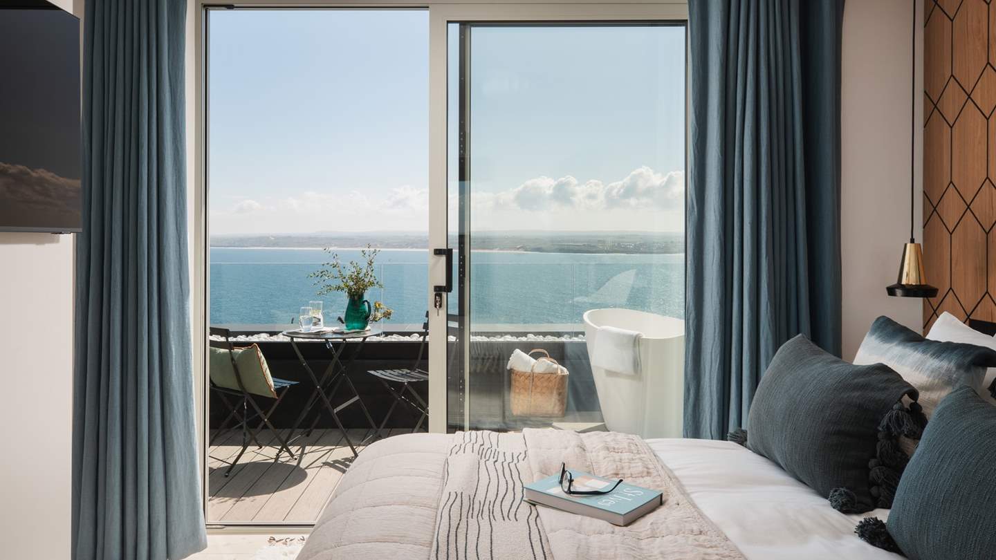 A sumptuous king size bed awaits in the first bedroom, with a soft blue headboard and geometric, timber-panelled feature wall