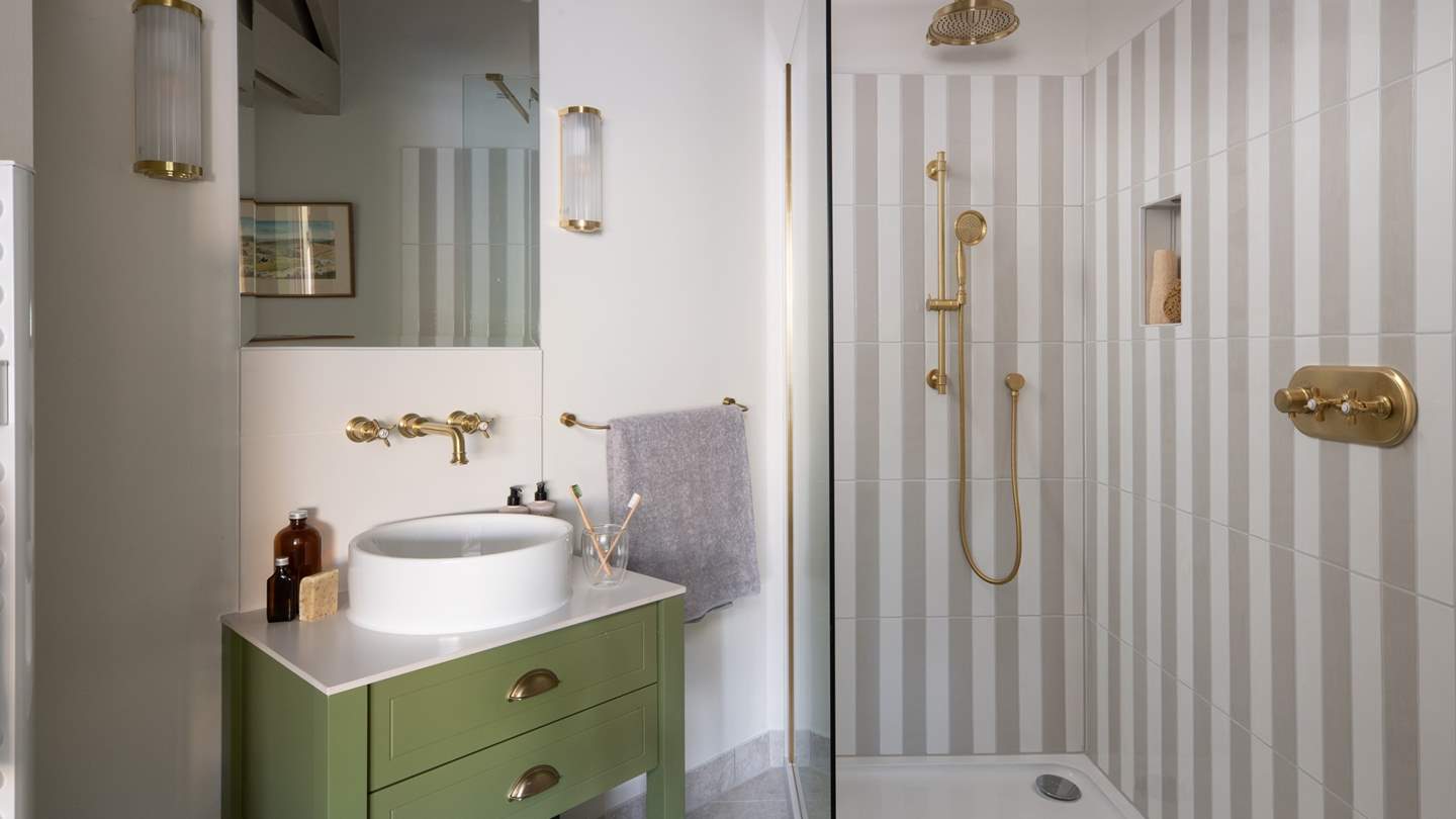 Open the sliding barn door to reveal a stunning ensuite shower room, with a sage green sink, brass detailing, and a large rainfall shower