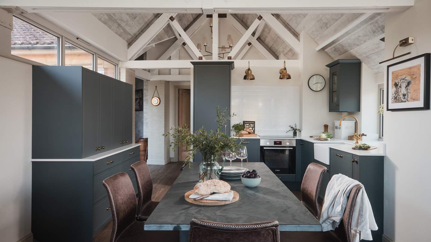 At the centre of the room, there is a dining table for six in sleek charcoal tones and soft suede chairs in rich chocolate shades
