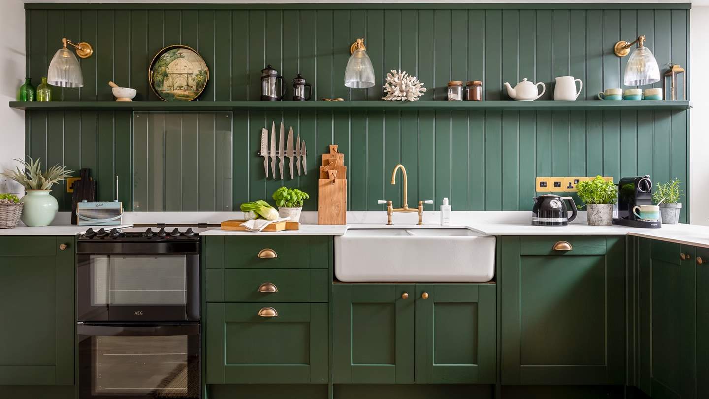 Forest green panelling and cupboards beautifully complement the crisp white worktops and chic brass detailing in the enchanting kitchen