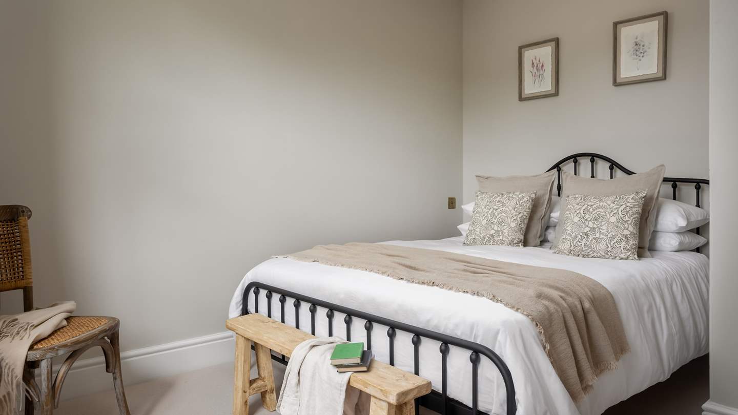 Soft greys permeate bedroom four, with a rustic rattan chair and wooden dresser adding a flicker of country charm