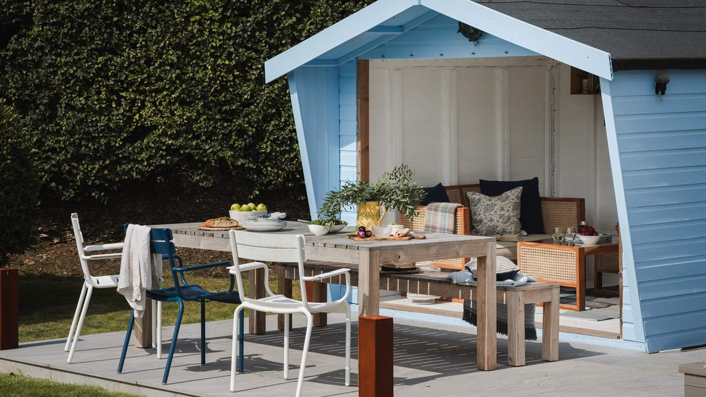 Inside the summerhouse, cosy seating and handsome furniture creates a beautiful hideaway in which to escape with a book and a glass of something special