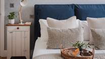 A navy king size bed draped in the finest linens and topped with cushions and throws rests below a tall, sloped ceiling

