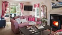 Adorned with pretty pink tones, the welcoming sitting room, surrounded by large windows, affords plenty of room for slow moments and easy living