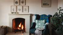 A comfortable armchair designed in traditional Scottish tartan is perfectly placed beside the open log fire