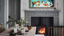 Warming the space is a wood burning stove set within a handsome grey mantelpiece, while eclectic artwork adds tasteful pops of colour throughout