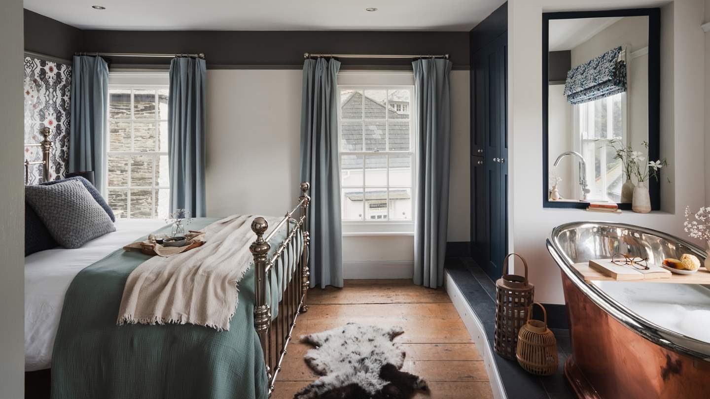 The king size bed bedecked in the finest linens rests beside a feature wall with Caspian wallpaper by Emma J Shipley and promises views over the roofs of the villages towards the sea