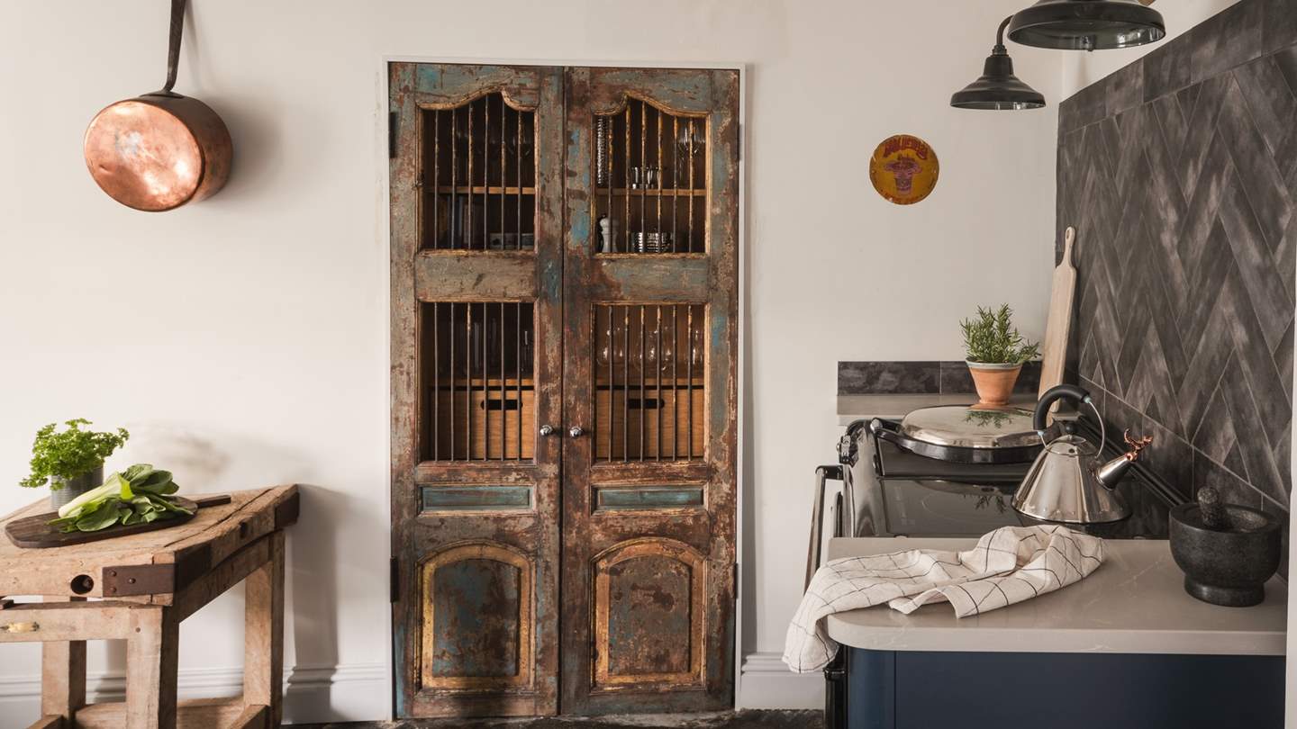 The pretty pantry framed by rustic, patina doors complements the kitchen’s floating white cupboards and grey herringbone splashback