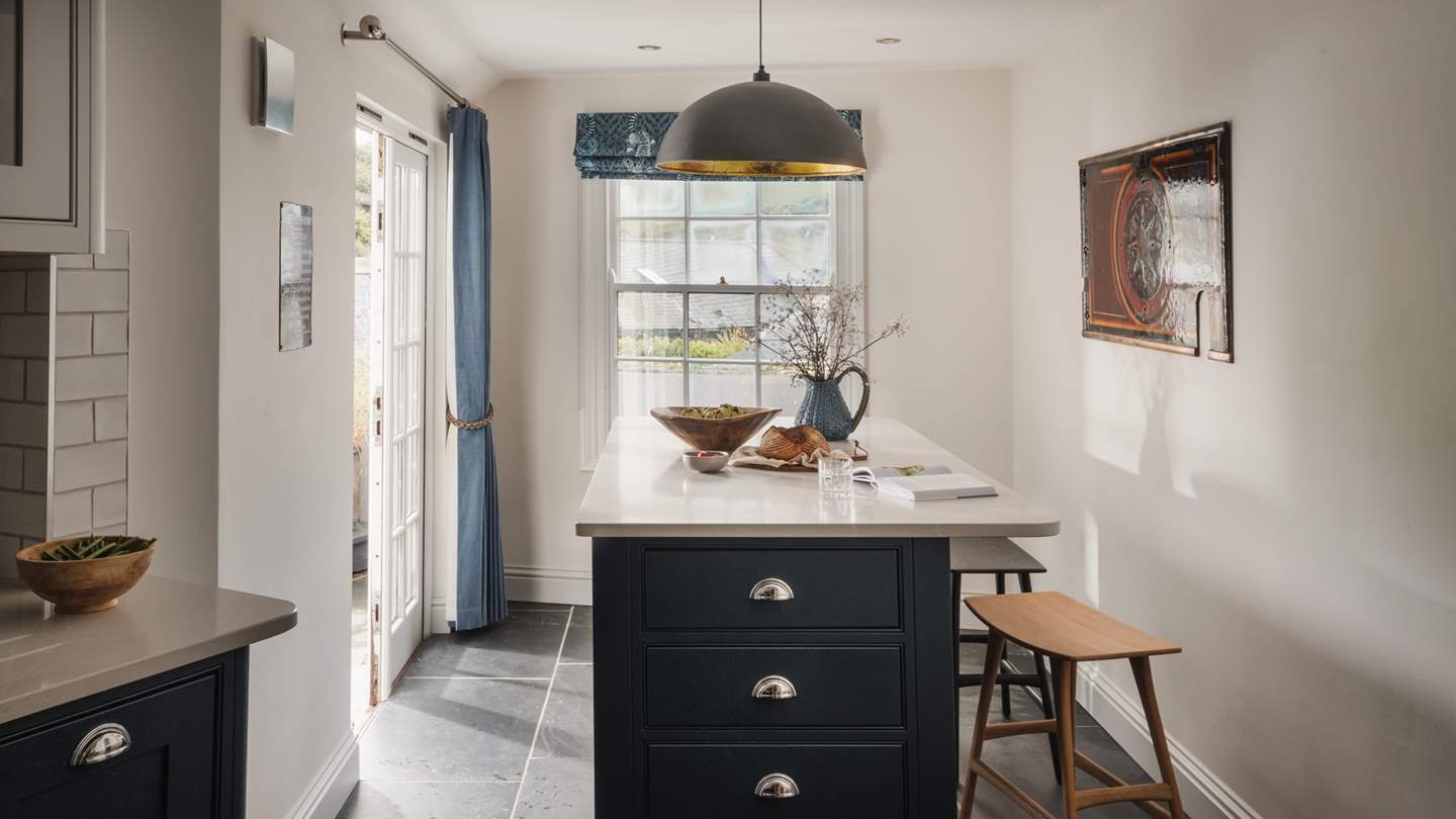 The kitchen island with stools occupies a sunlit space next to glass patio doors and is illuminated by a striking statement hanging lamp