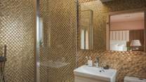 The shower room is adorned in scalloped glass tiles in lustrous shades of gold