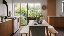 The mid-century kitchen and dining space is filled with natural light and looks out to verdant garden foliage