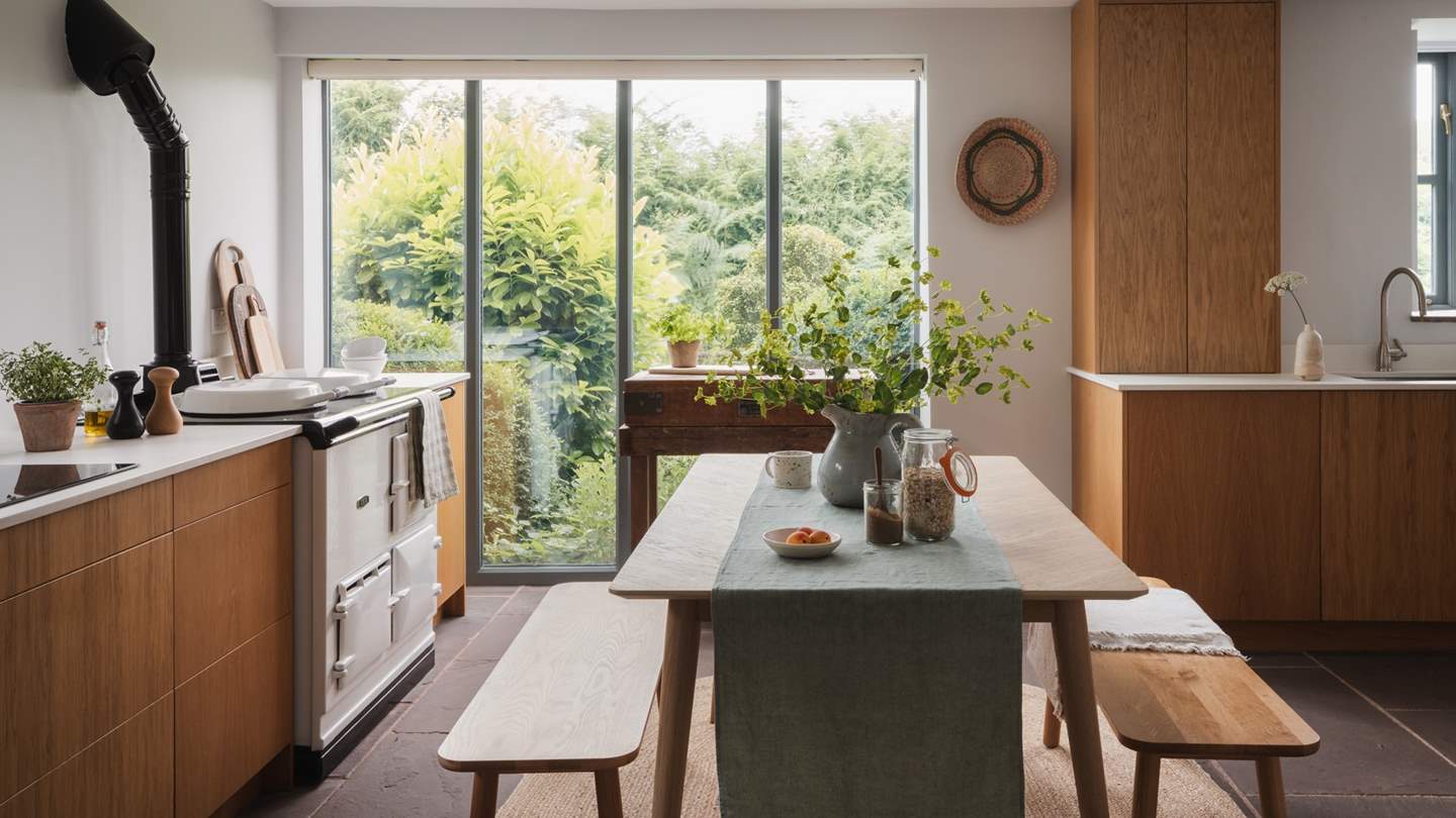 The mid-century kitchen and dining space is filled with natural light and looks out to verdant garden foliage