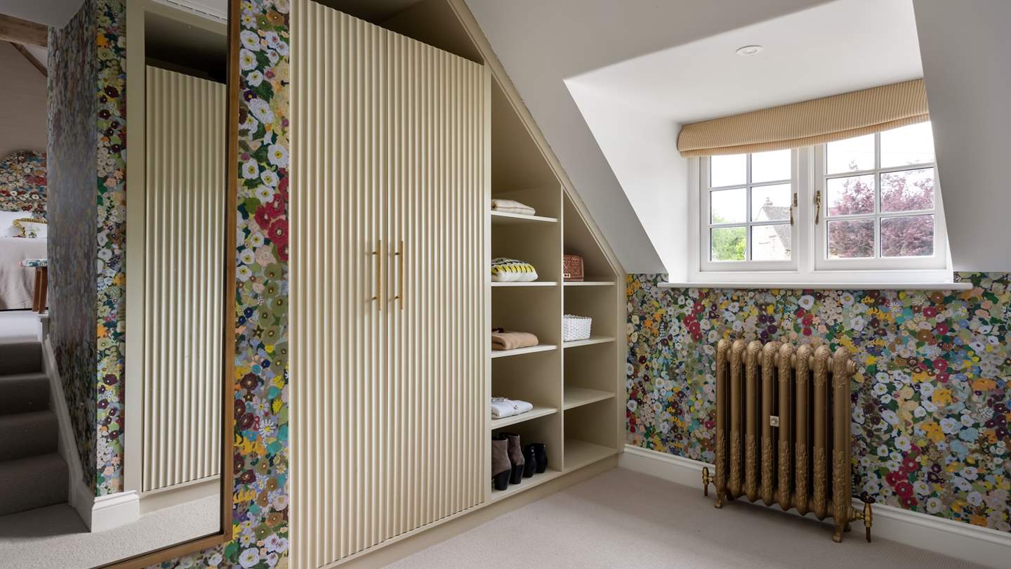 Down a short flight of stairs is a spacious dressing room with built-in wardrobes and Hollyhocks floral wallpaper by House of Hackney