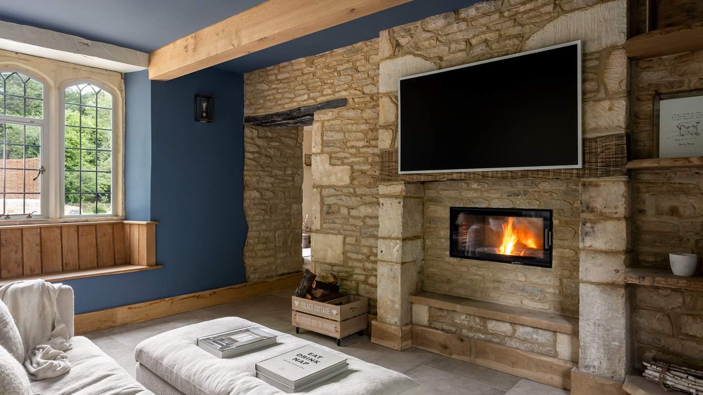 An exposed stone feature wall and a contemporary dual sided wood burning stove create a cosy space for all to gather in style