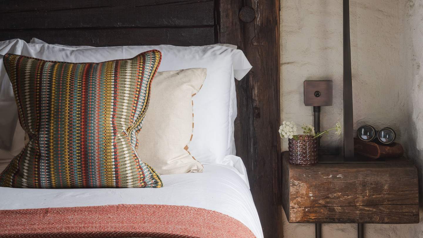 A king-size bed with stained-wood headrest is dressed in the finest linens 