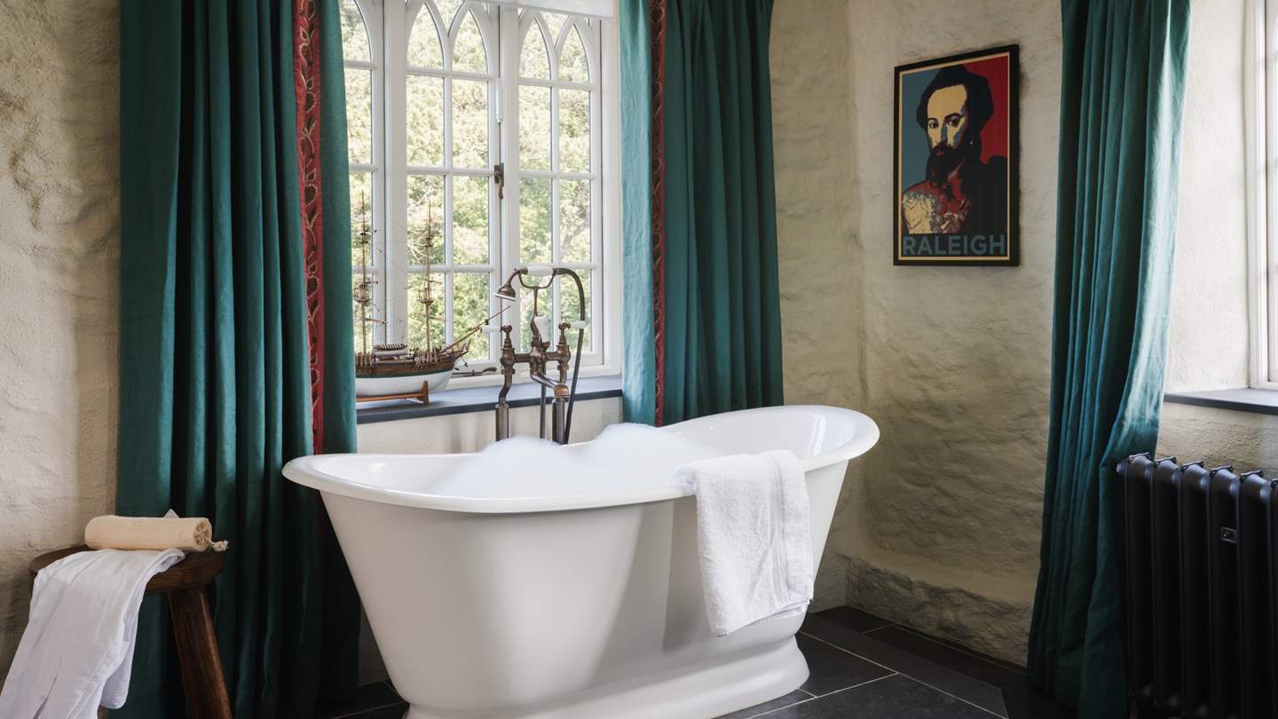 An elevated, free-standing, roll top bath rests beside riverside views 