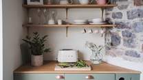 Integrated moss green cabinets with an oak counter sit within a pretty alcove and adorned wooden shelves
