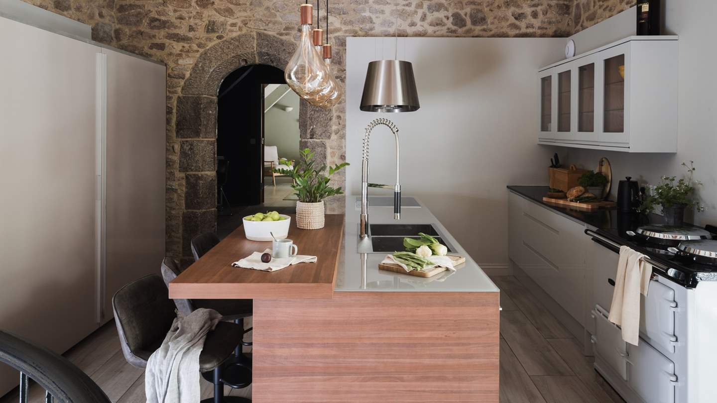 A dream for culinarians, it features sleek, white handleless cabinetry and a wood kitchen island topped with a glass counter