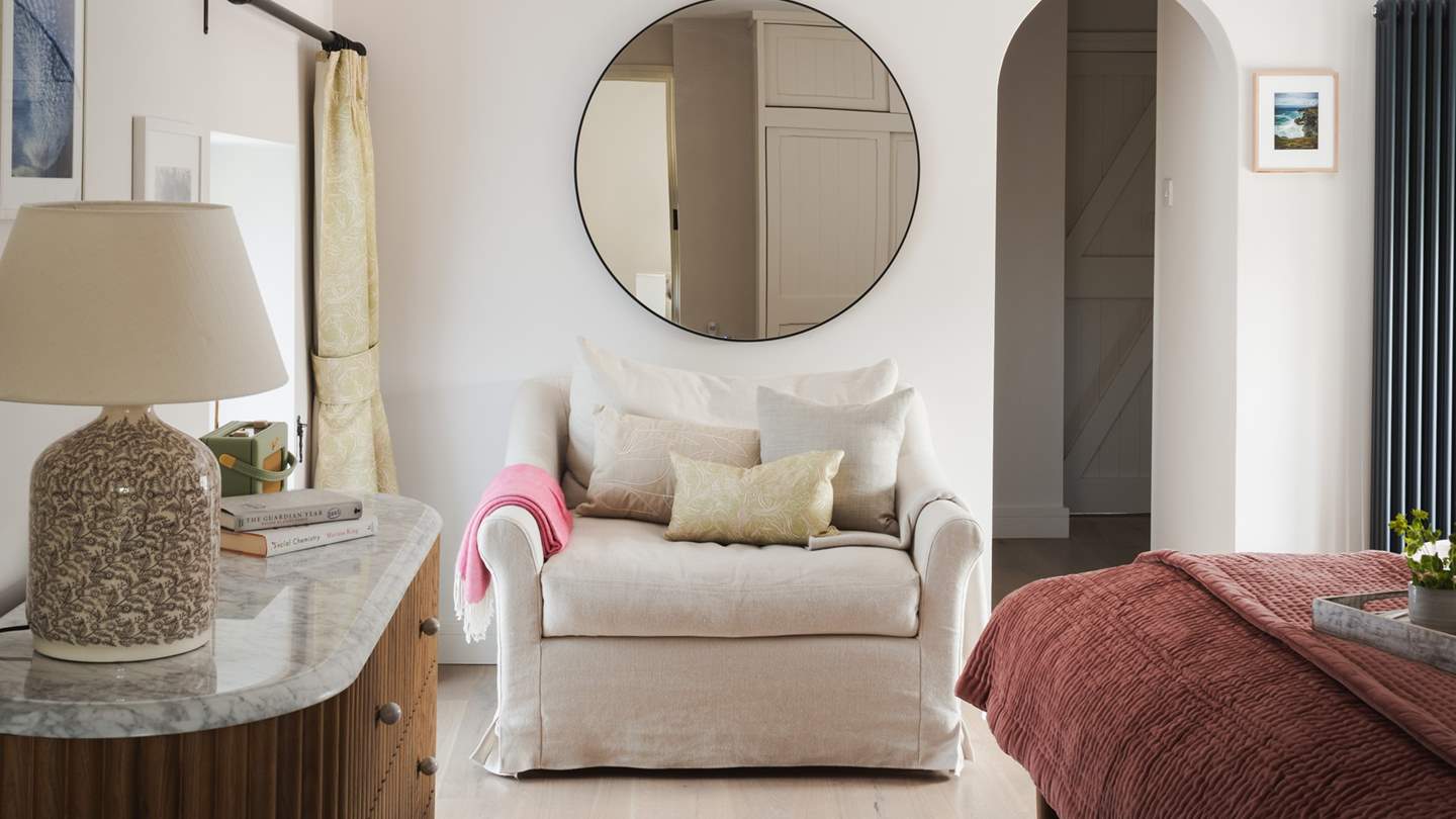 A large oat linen loveseat provides a place to cosy up with a book next to a glass door which opens directly onto the garden