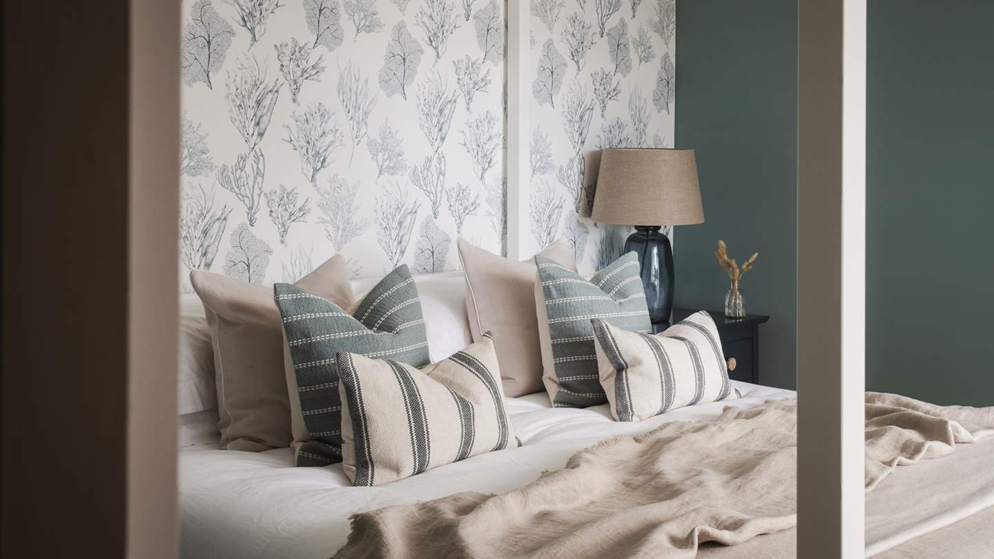 In four-poster grandeur, a super-king bed takes pride of place in the centre of the room, coupled with navy bedside tables and a wooden bench
