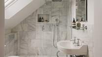 The en suite shower room with a walk-in rainfall shower is adorned with luxe marble tiles